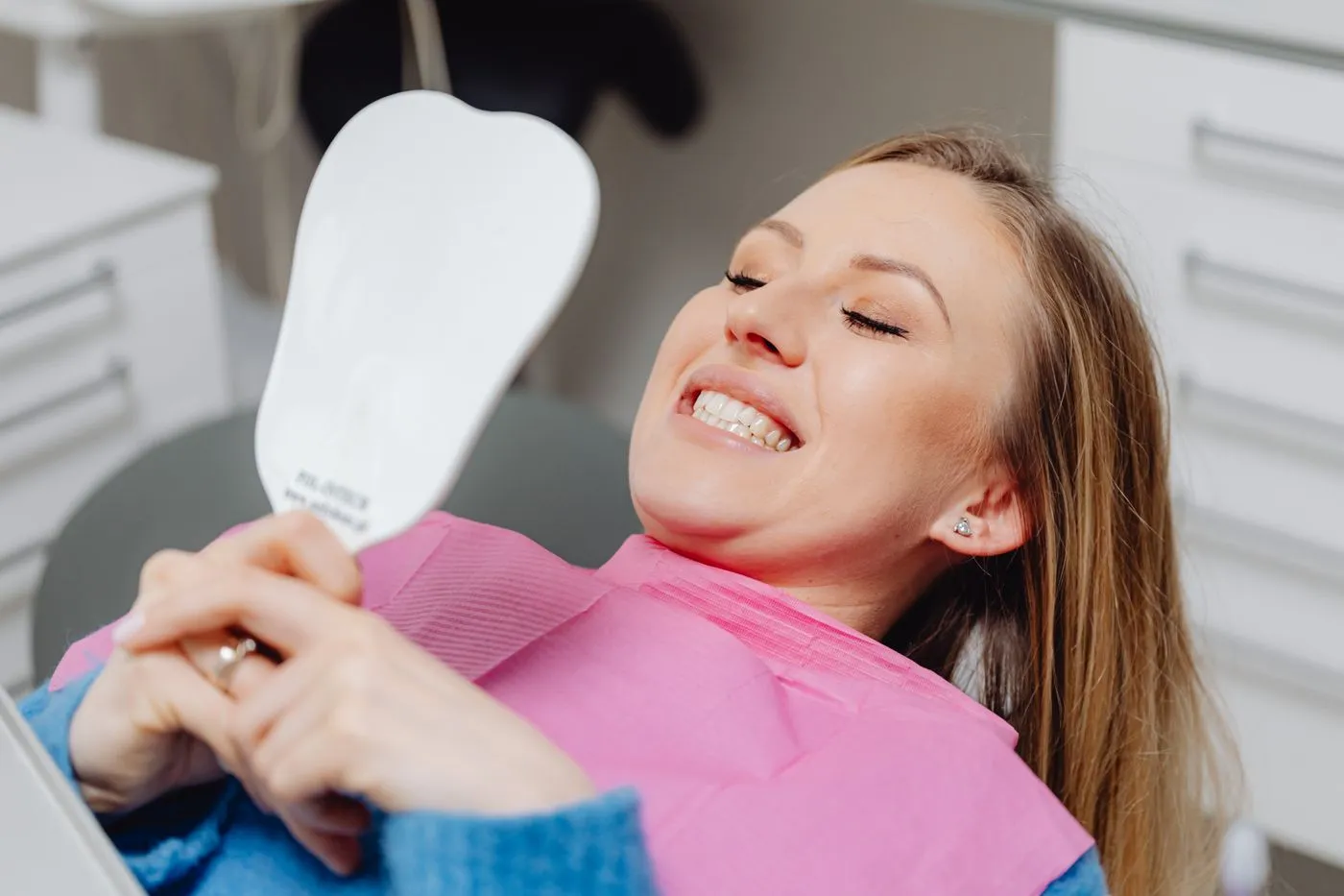 A patient smiling at her teeth in a hand mirror after treatment